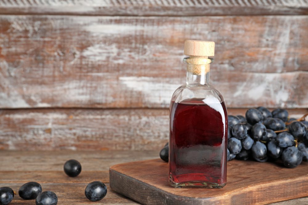 Bottiglia di vetro con aceto di vino e uva fresca su un tavolo di legno